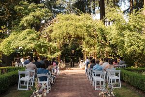 White chairs line a tree-shaded outdoor garden path for an elegant wedding ceremony setup.
