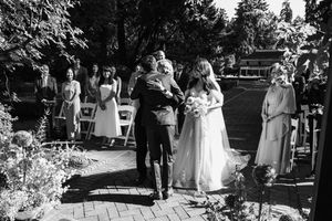 Outdoor garden wedding ceremony setup with white chairs arranged on a lawn surrounded by trees.