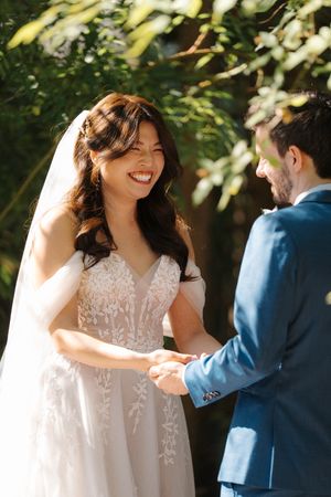 Joyful outdoor wedding ceremony featuring couple exchanging vows under trees on a sunny day.