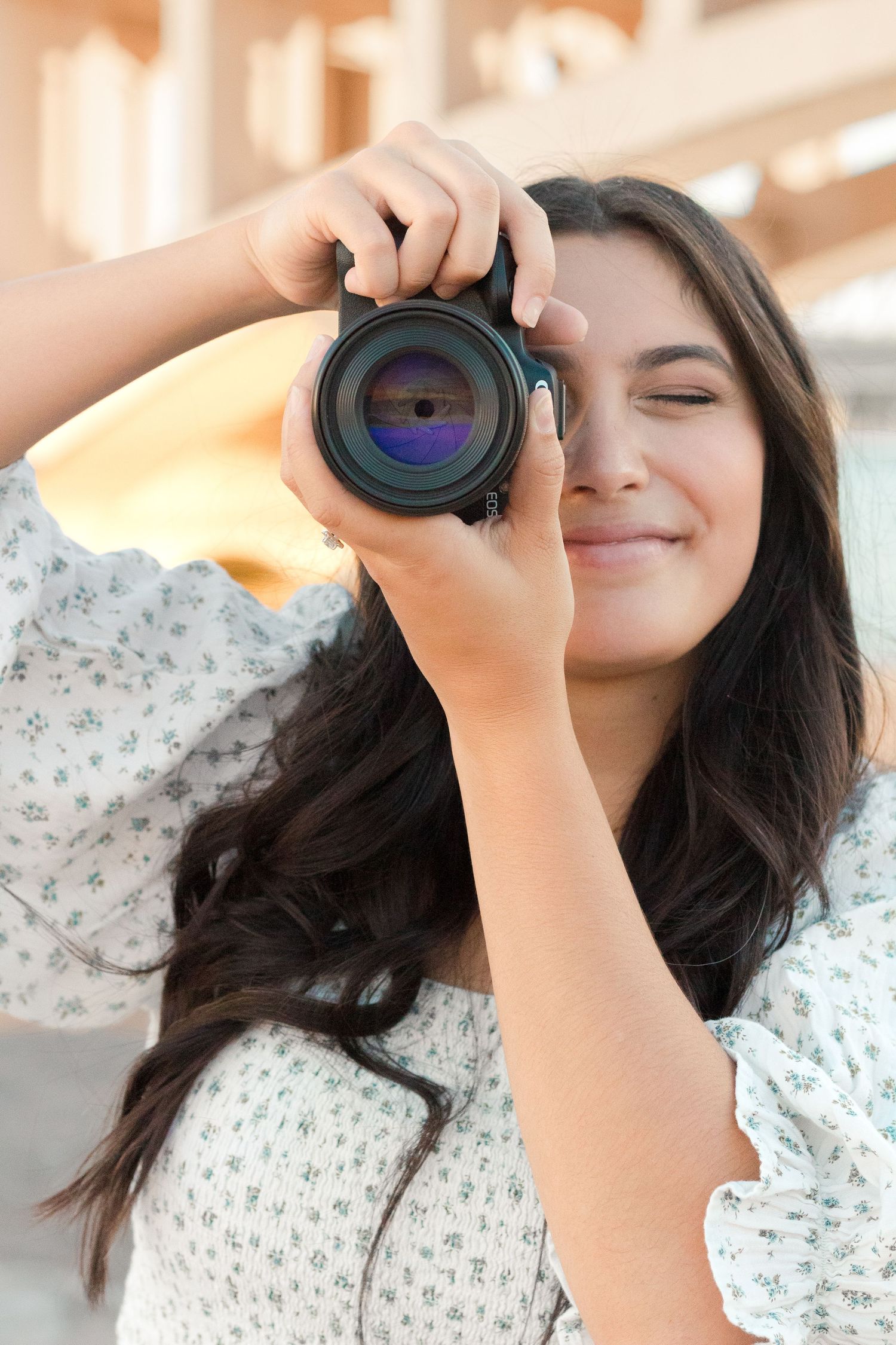 Young woman photographer holding camera up to eye in an Ivy City Co floral dress as a light and airy family photographer in Gilbert, Arizona