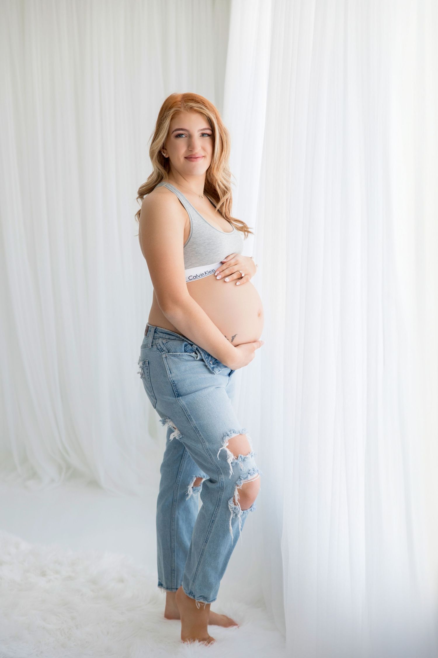 Artistic maternity portraits featuring woman in light denim and gray top against white curtains.