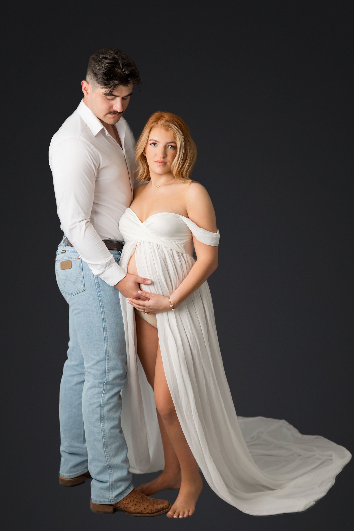 Dramatic maternity photos against black background with flowing white dress and denim.