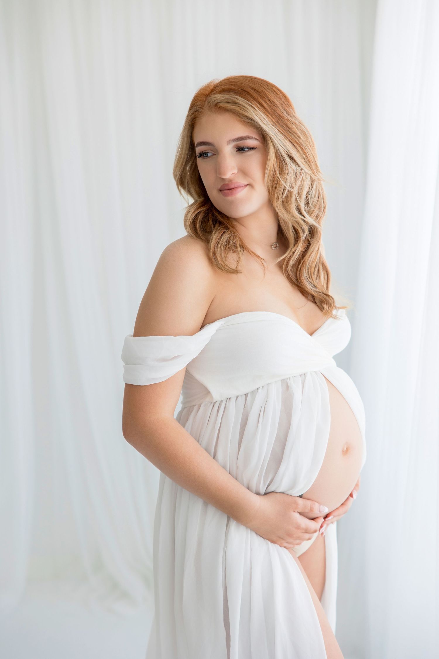Ethereal maternity portraits in white flowing dress against soft natural light background create dreamy romantic aesthetic.
