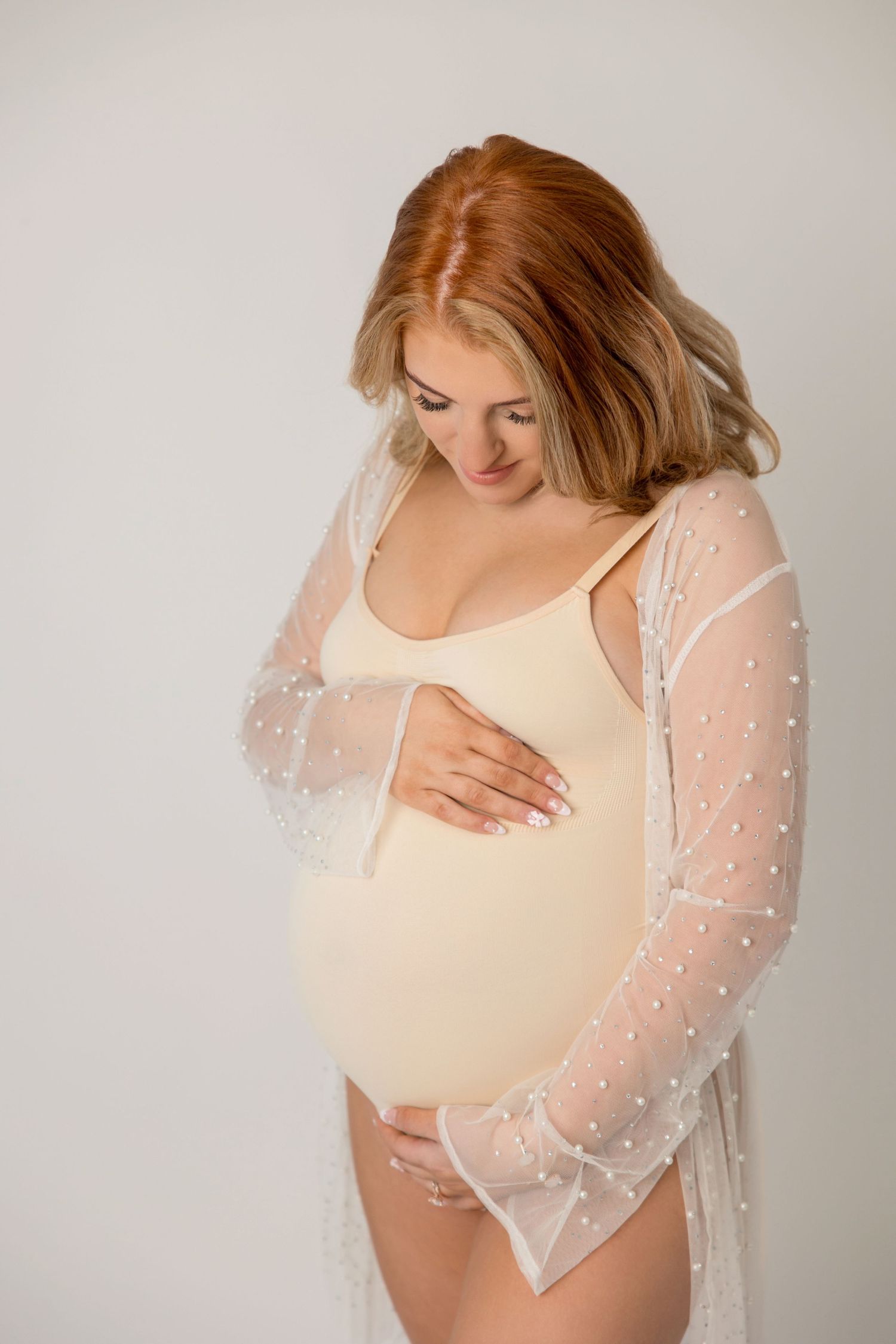 Dreamy maternity photos showing person in sheer overlay with sparkly details against light background.