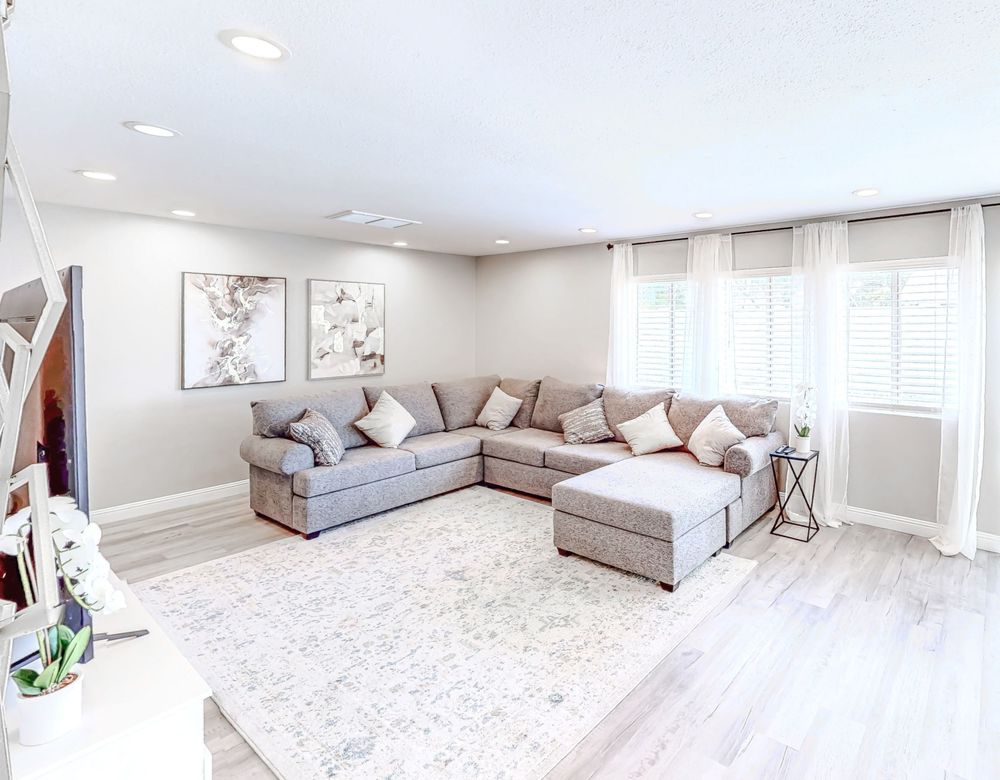 Bright living room with panoramic windows, light grey sofa, and white carpet.