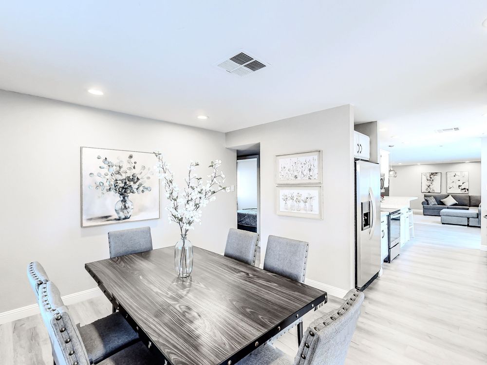 Modern apartment interior with white walls, grey sectional sofa, and hardwood dining table.