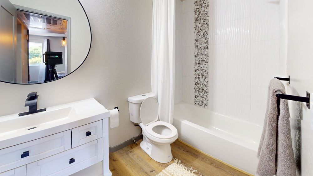 Contemporary bathroom with round mirror, white fixtures, and mosaic tile accents.