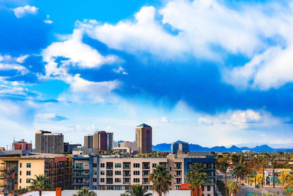 phoenix skyline with modern buildings against blue sky with white clouds and mountain backdrop.