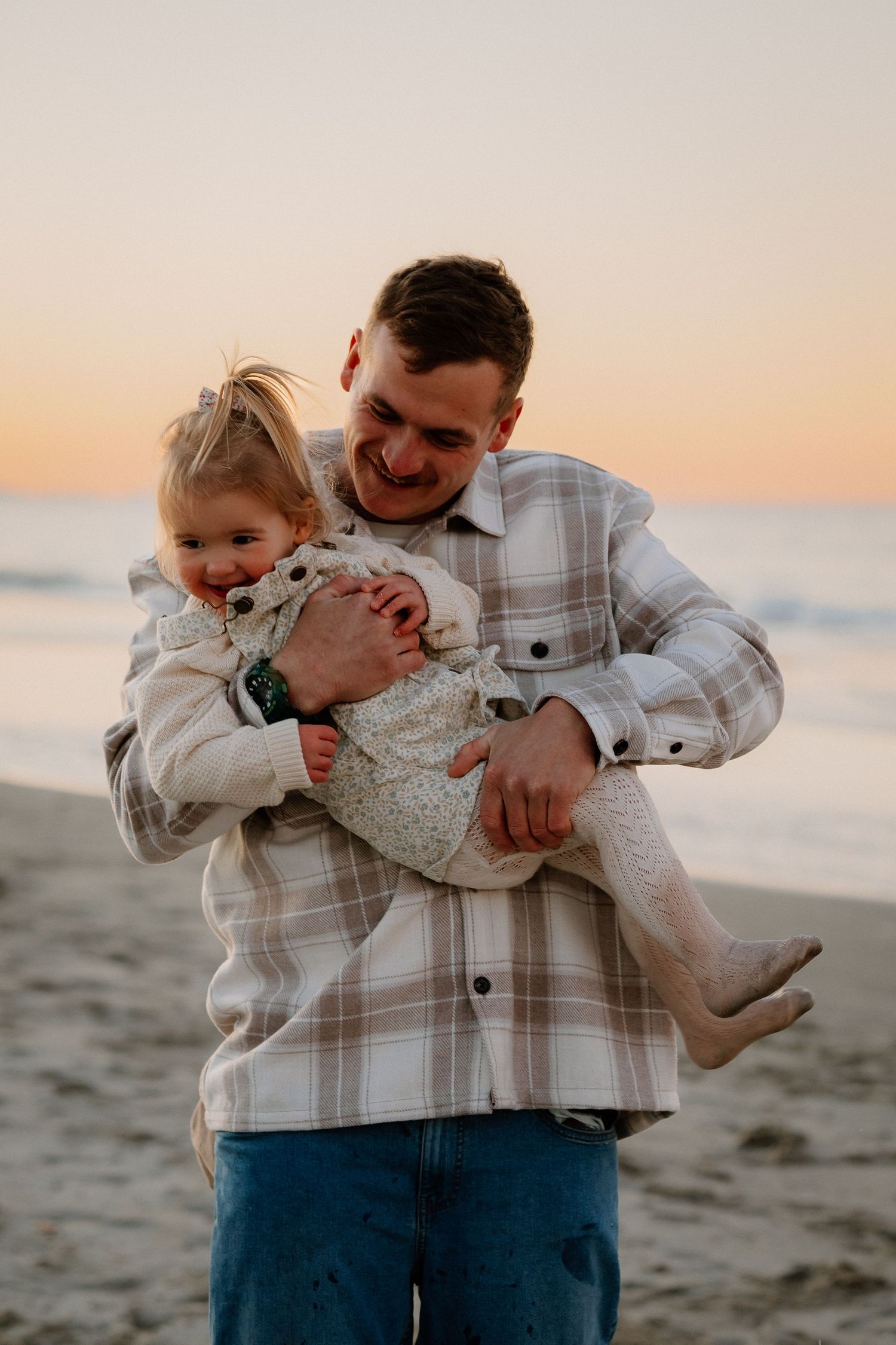 A loving moment captured between a parent and child playing together on a sandy beach at sunset.