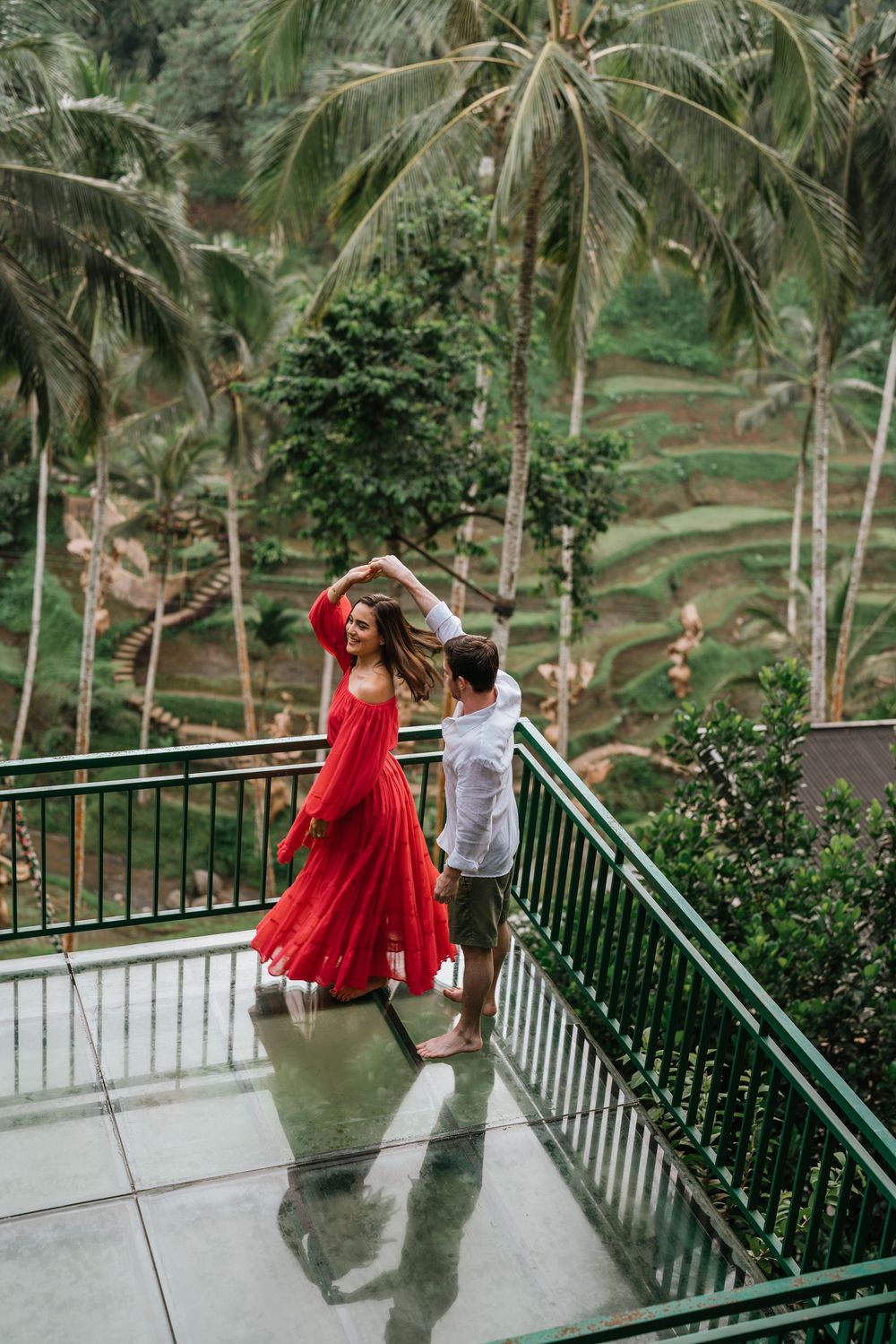 A couple dancing together on a terrace overlooking lush tropical rice terraces and palm trees in Bali.