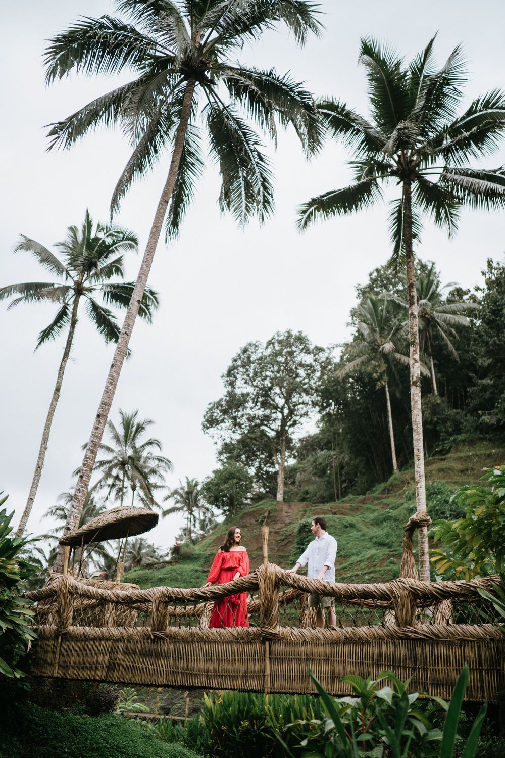 A romantic scene on a bamboo bridge surrounded by towering palm trees in a tropical landscape.