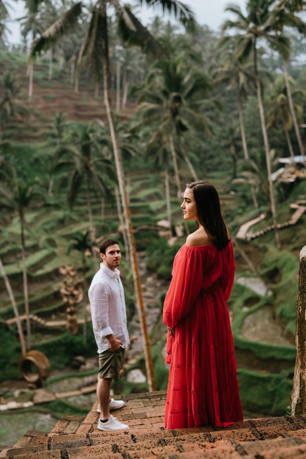 A romantic couple poses among terraced rice fields and palm trees in Bali's countryside.
