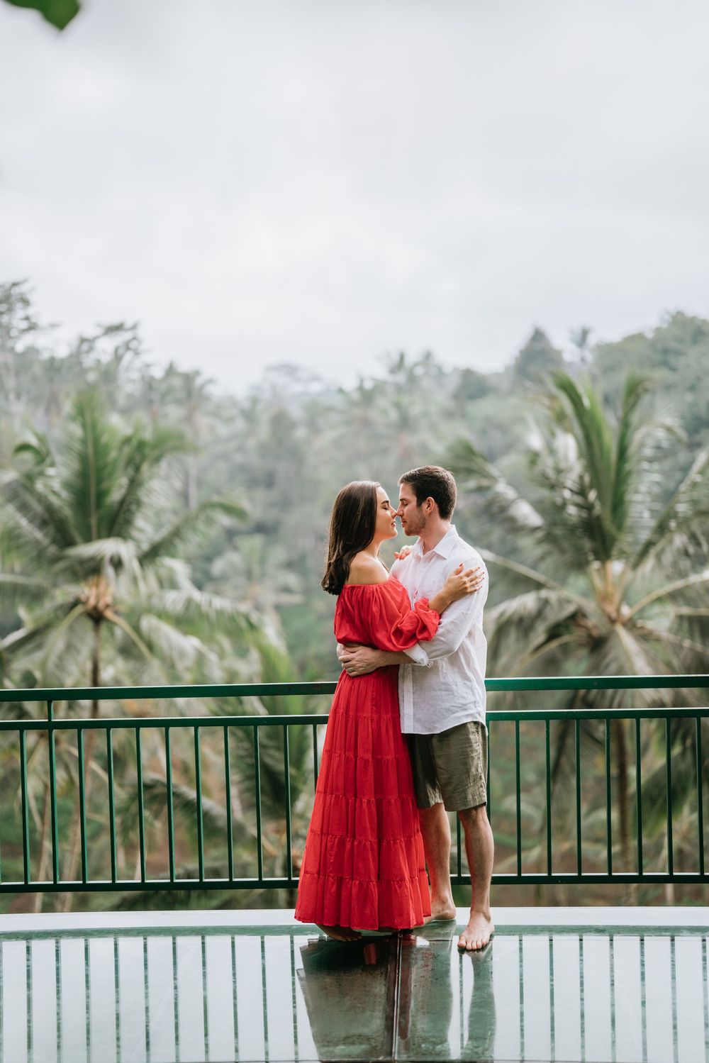 A couple embraces on a wet deck overlooking a tropical palm forest landscape.