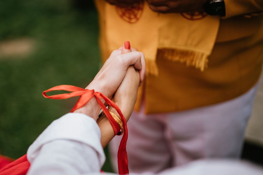 Close up of hands tied together with red ribbon during traditional ceremony.