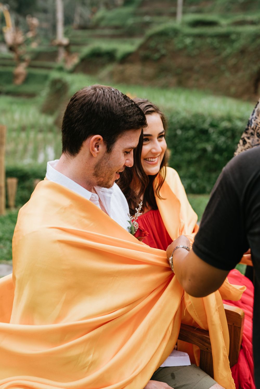 Couple wrapped in orange ceremonial cloth during traditional Balinese blessing ceremony.