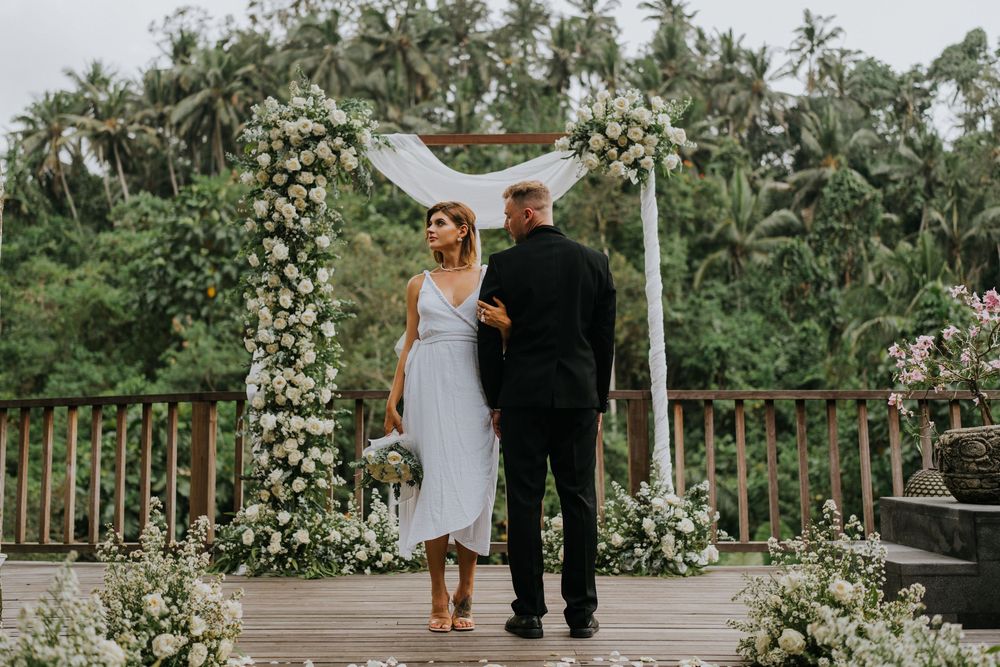 Wedding couple walking along a wooden deck decorated with white flowers and tropical foliage.