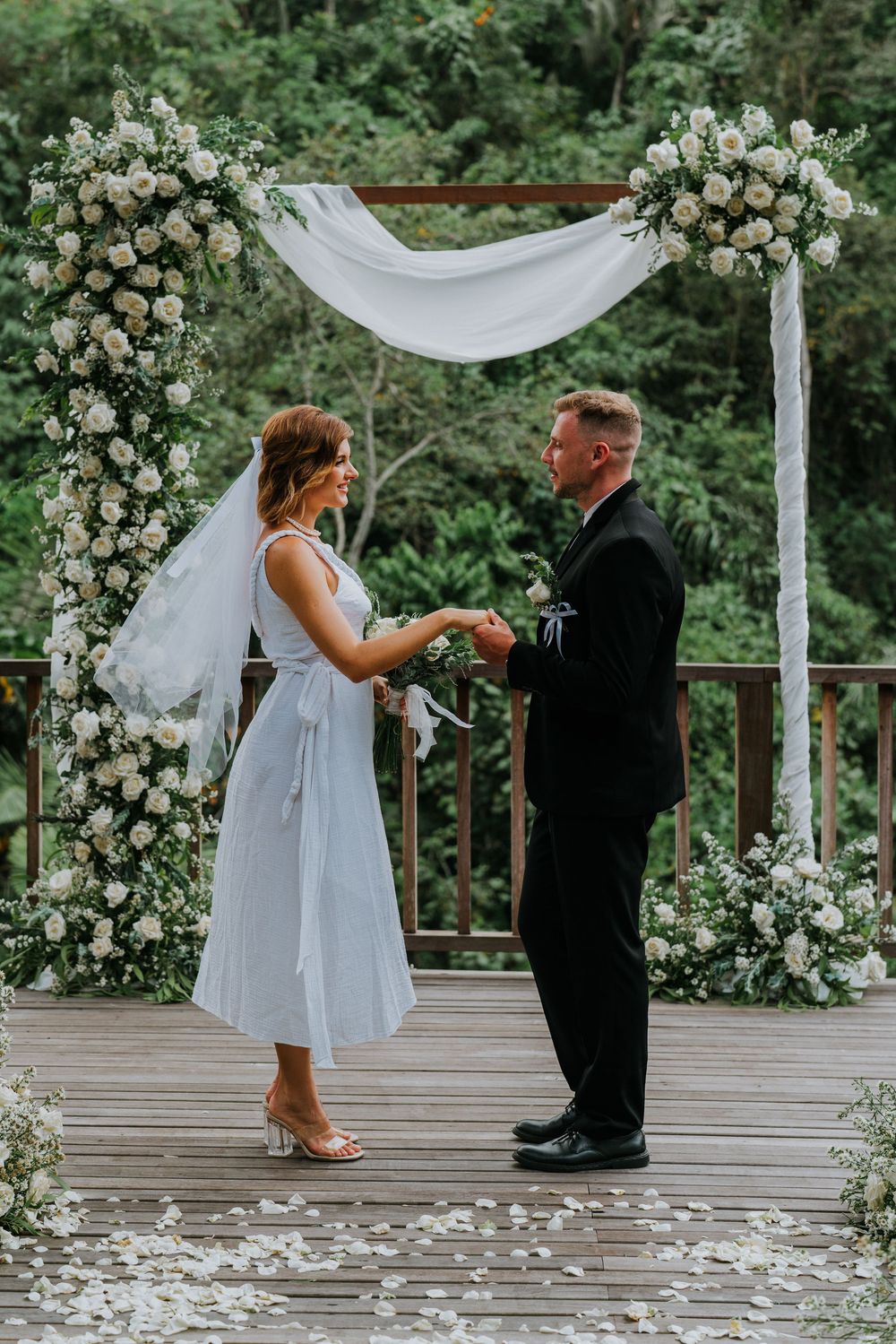 Wedding ceremony on wooden deck decorated with white floral arrangements and fabric draping.