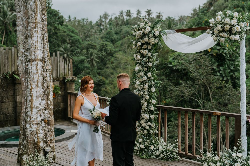 Outdoor wedding venue with white floral arch and wooden railings overlooking nature.