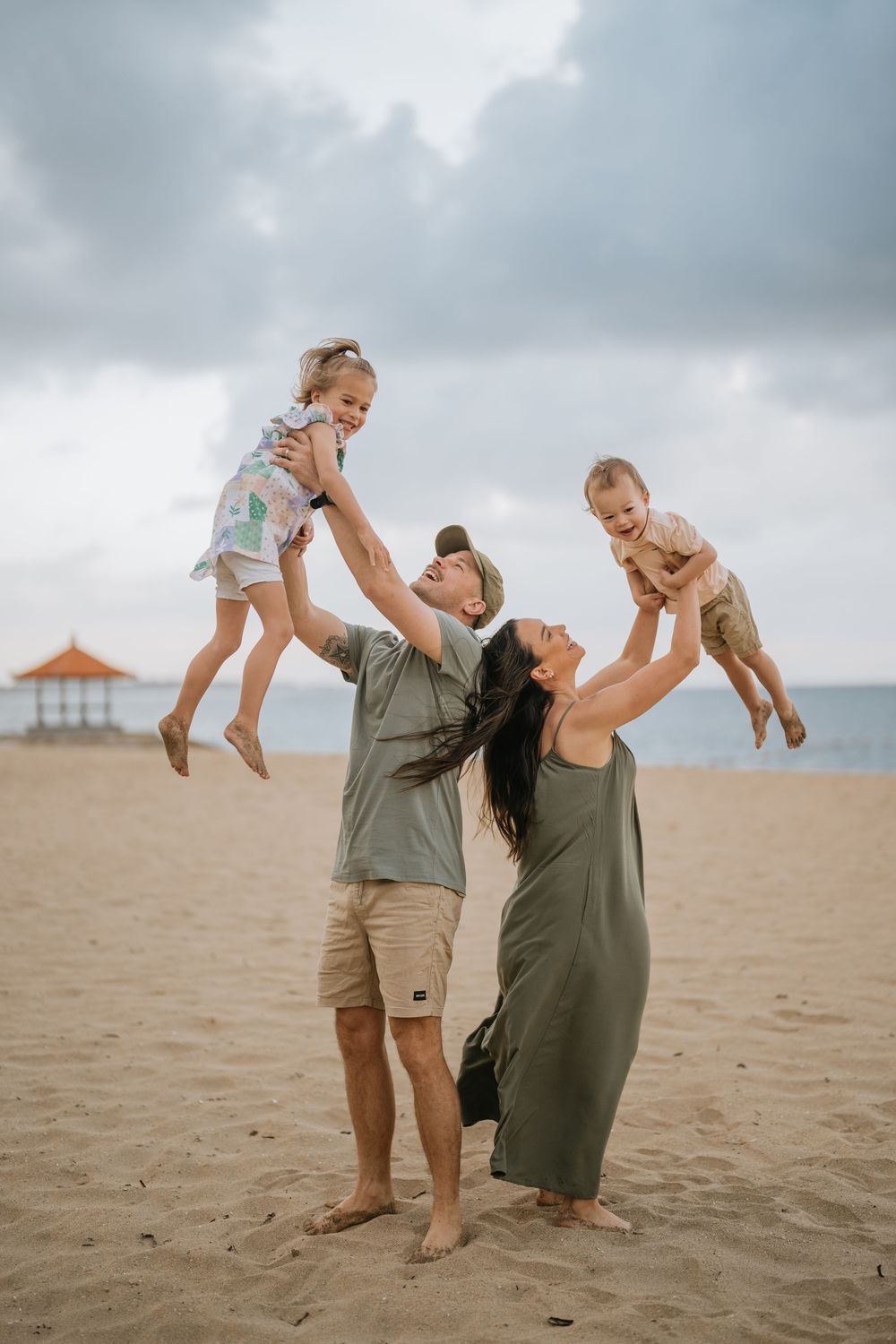 Playful moments captured on a beach with cloudy skies and ocean backdrop.