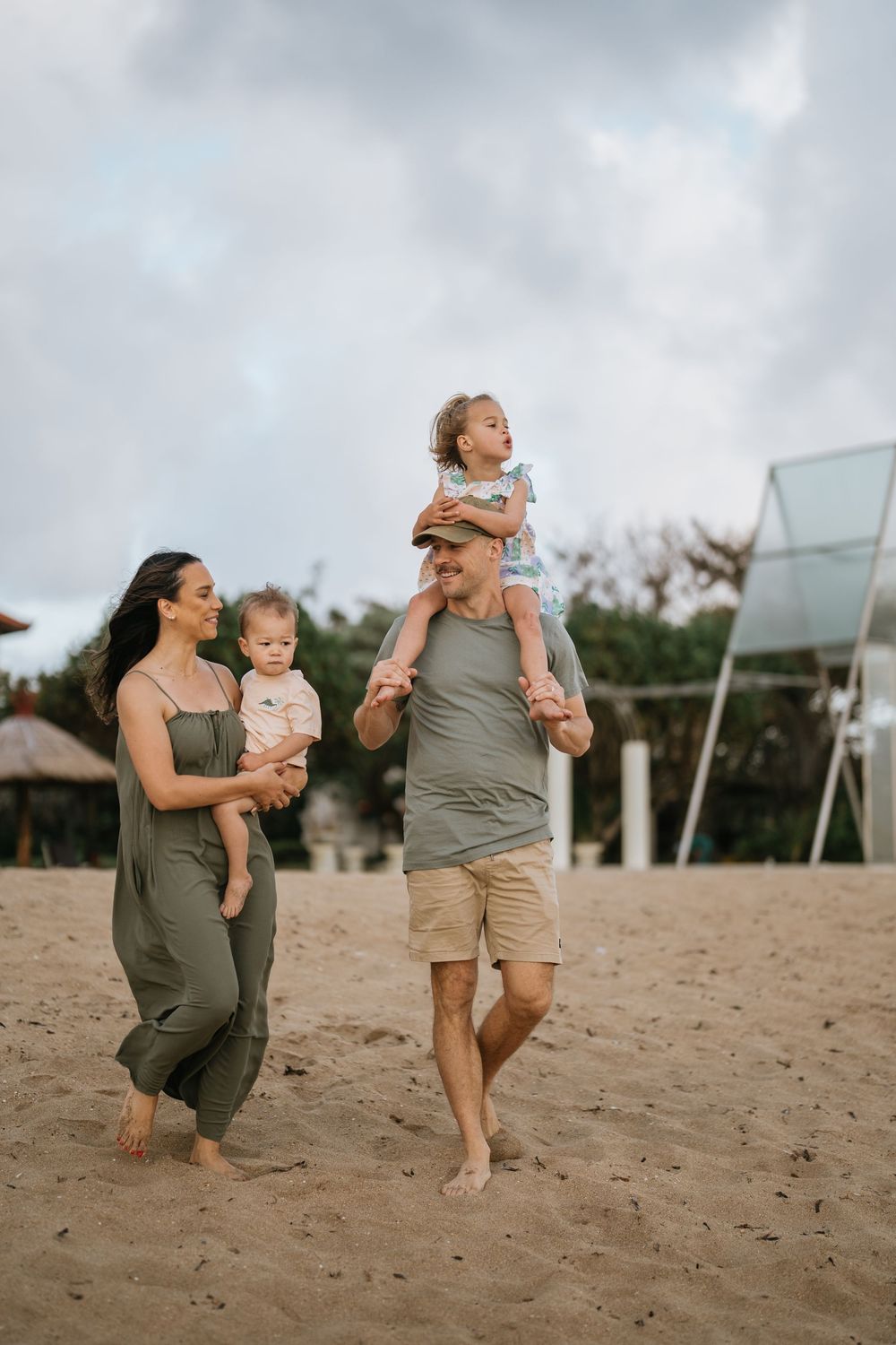 Family playing and laughing together on a sandy beach with overcast skies.
