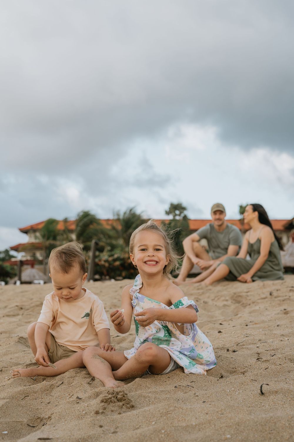 Children playing in the sand on a beach with buildings visible in the background.