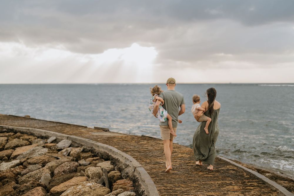 Family exploring rocky coastline under cloudy skies near the ocean.