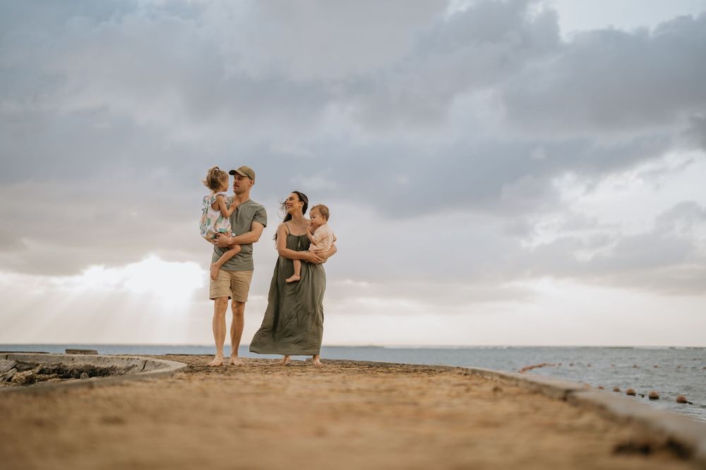 Silhouettes against cloudy sky on beach with ocean in background.