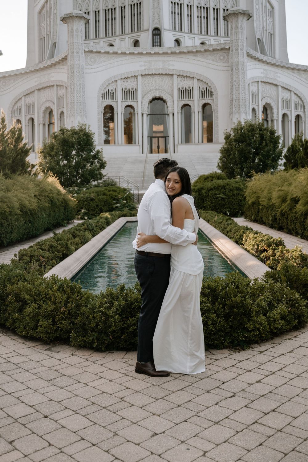 Couple shares a romantic moment in front of the Baha'i House of Worship with its ornate white architecture and gardens.