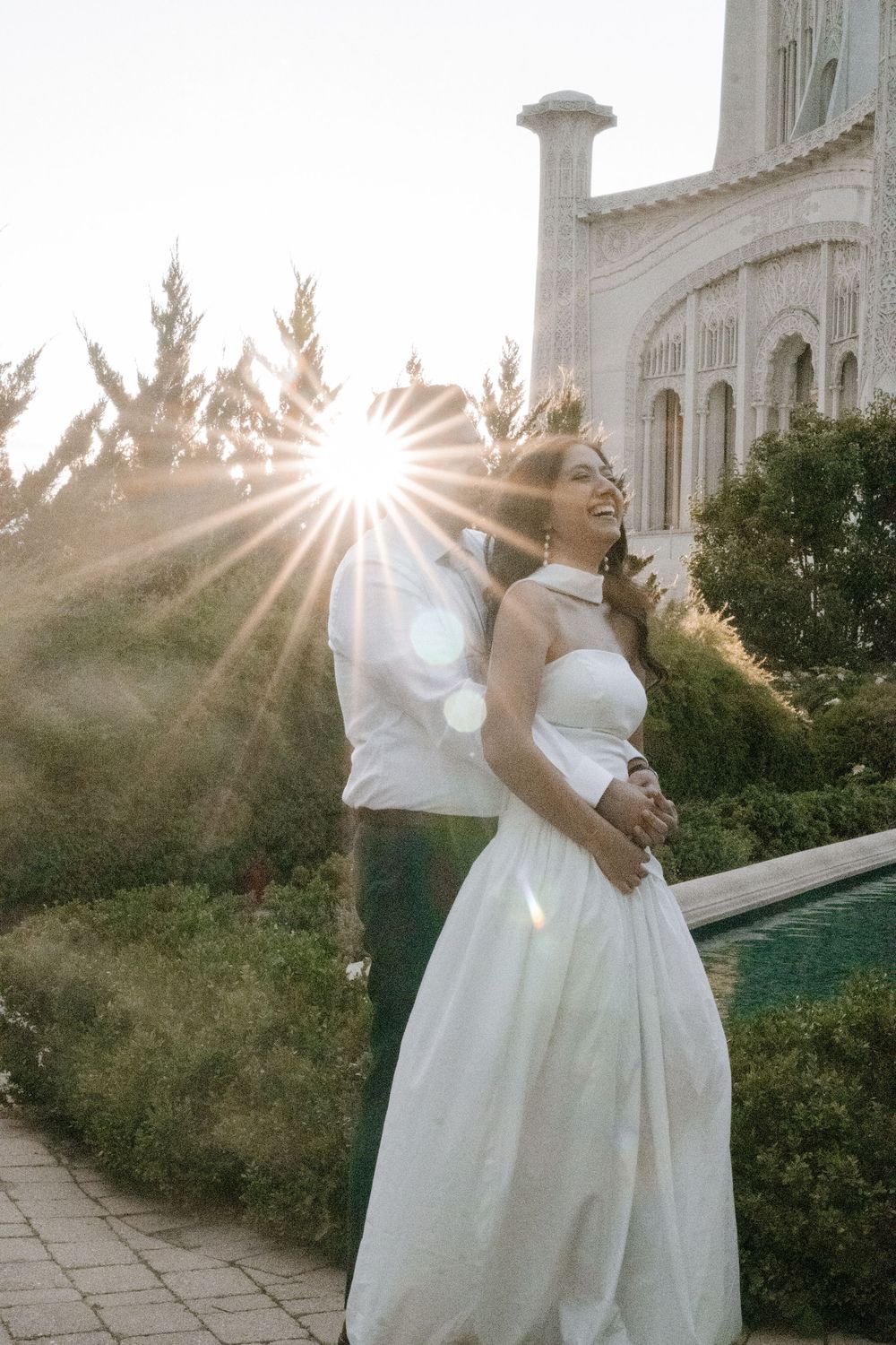 A romantic sunset engagement photo session outside a grand stone building with dramatic sunbursts.