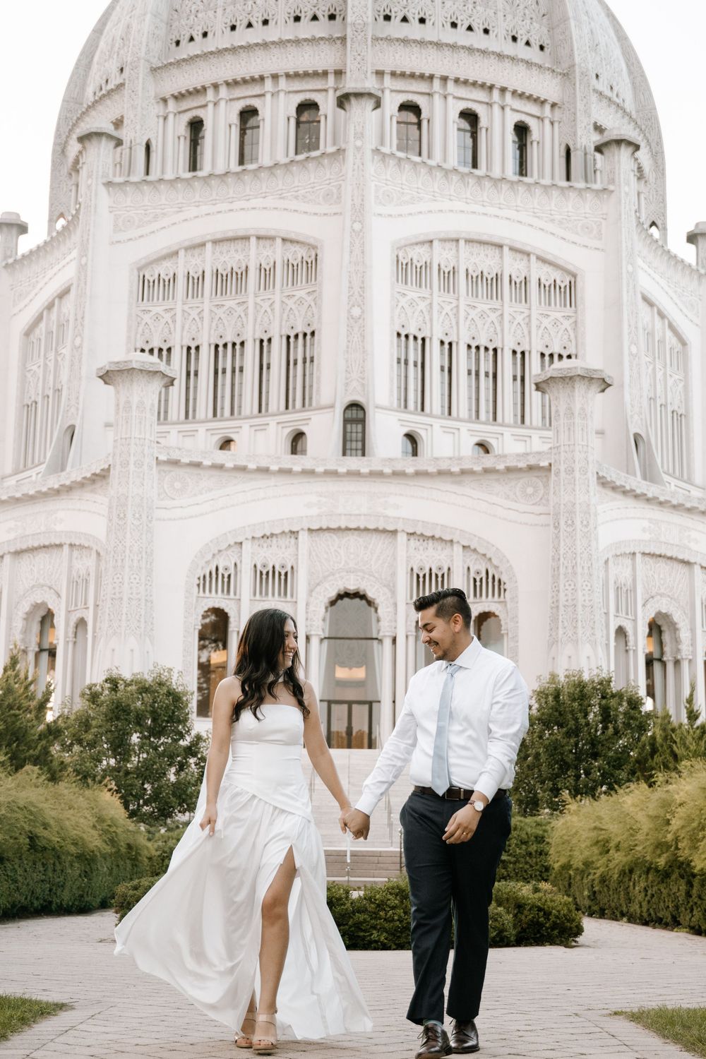 A couple in wedding attire walking on a path in front of the majestic Baha'i Temple in Wilmette, Illinois.