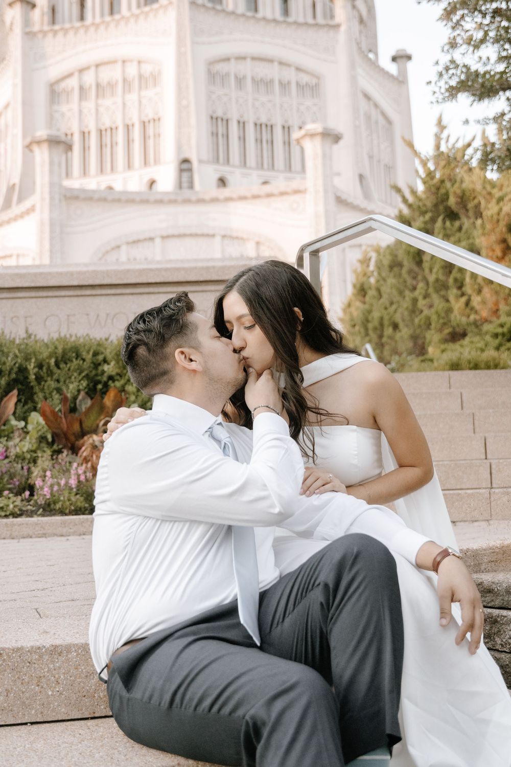 Romantic newlyweds share intimate kisses in front of an elegant white building on their wedding day.