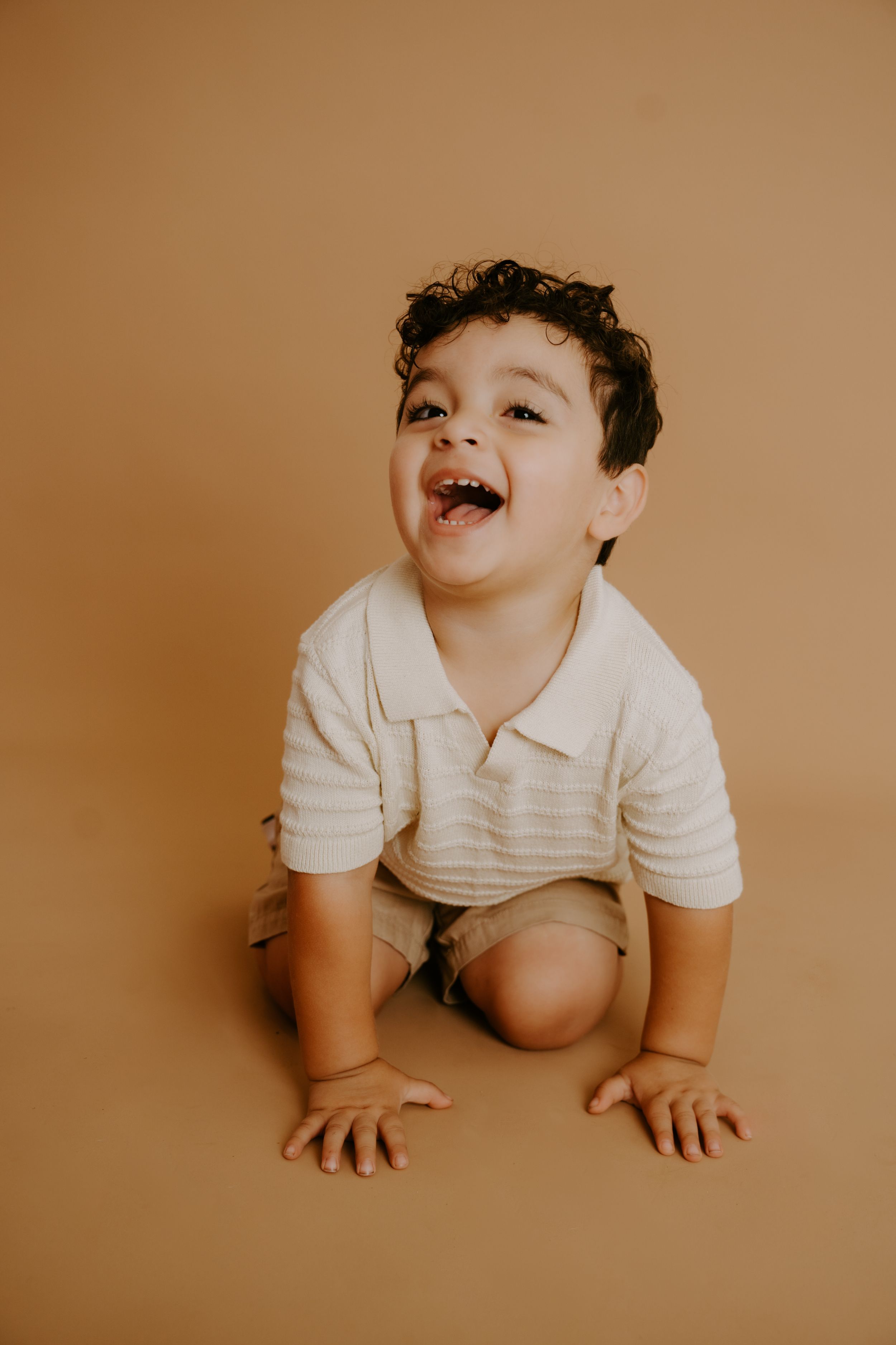 A laughing toddler in white clothing crawling on a brown background.