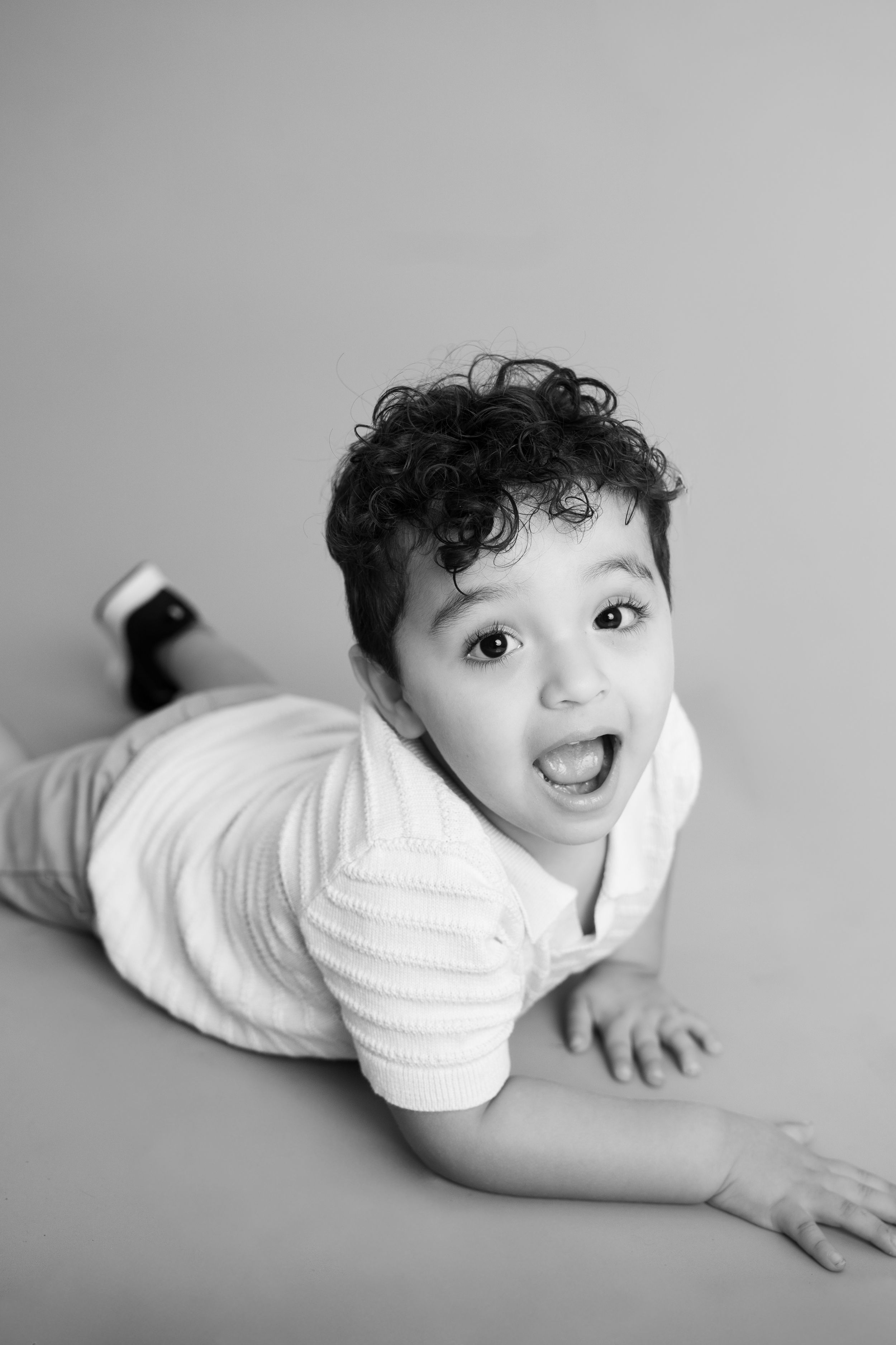 Black and white photo series of a baby in white clothing crawling and smiling on a light background.