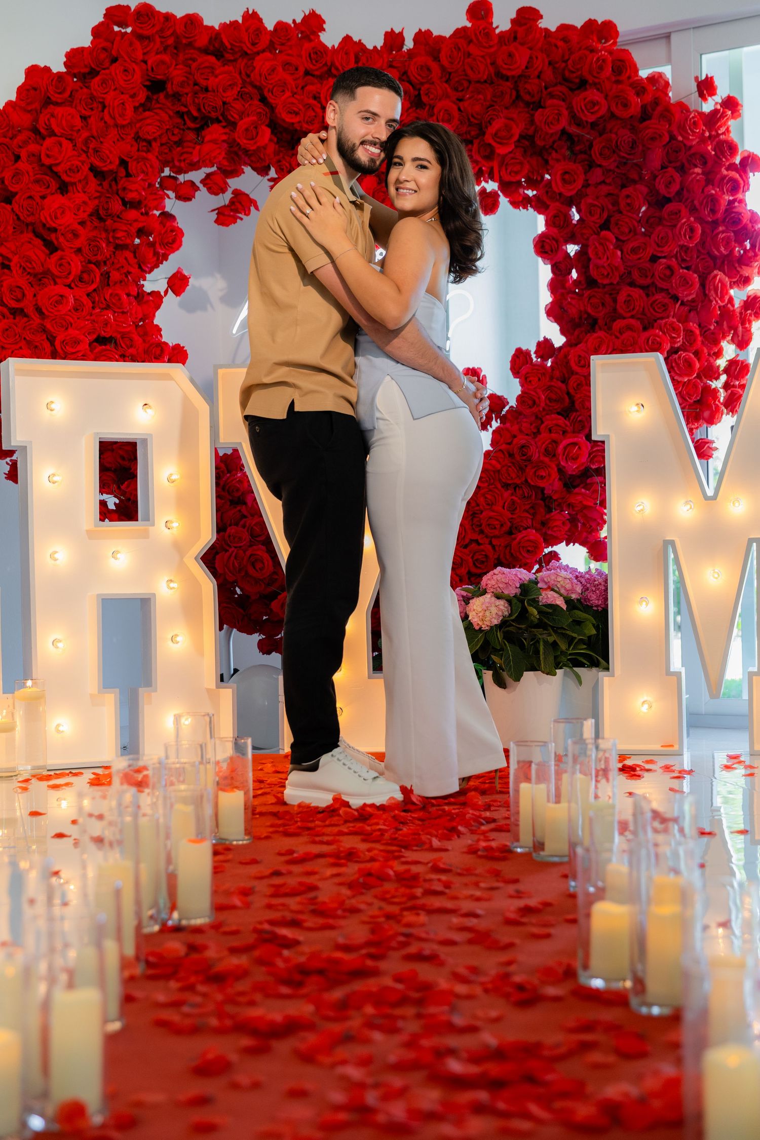 An elegant marriage proposal setup with lit MARRY ME letters framed by a dramatic red rose archway.