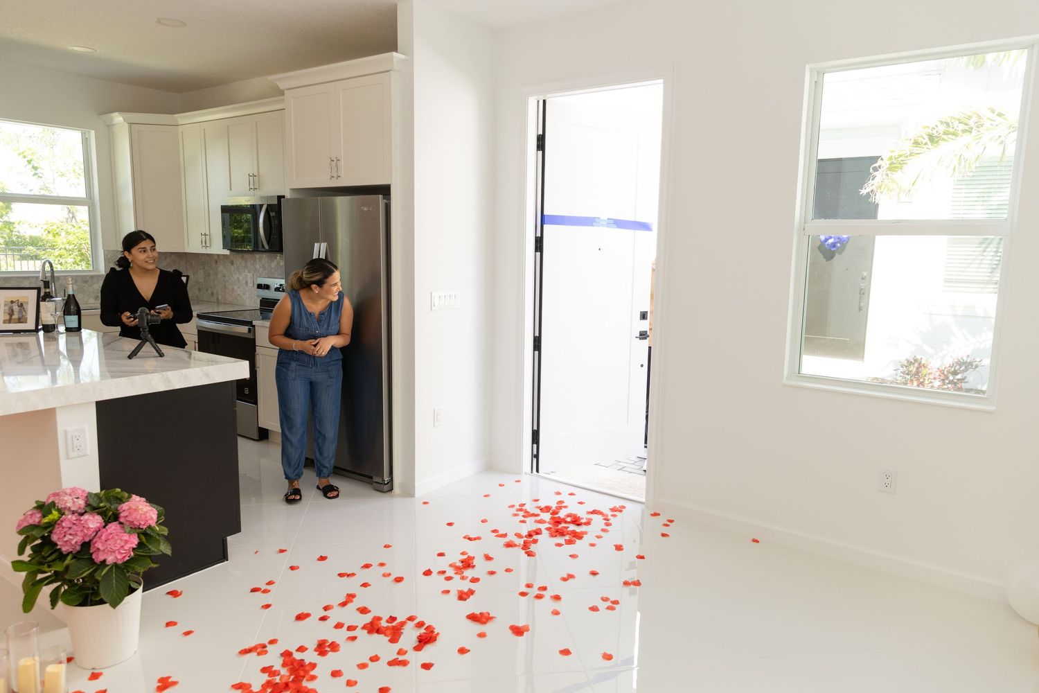 A romantic trail of red rose petals leads through a bright white interior space with multiple windows and doorways.