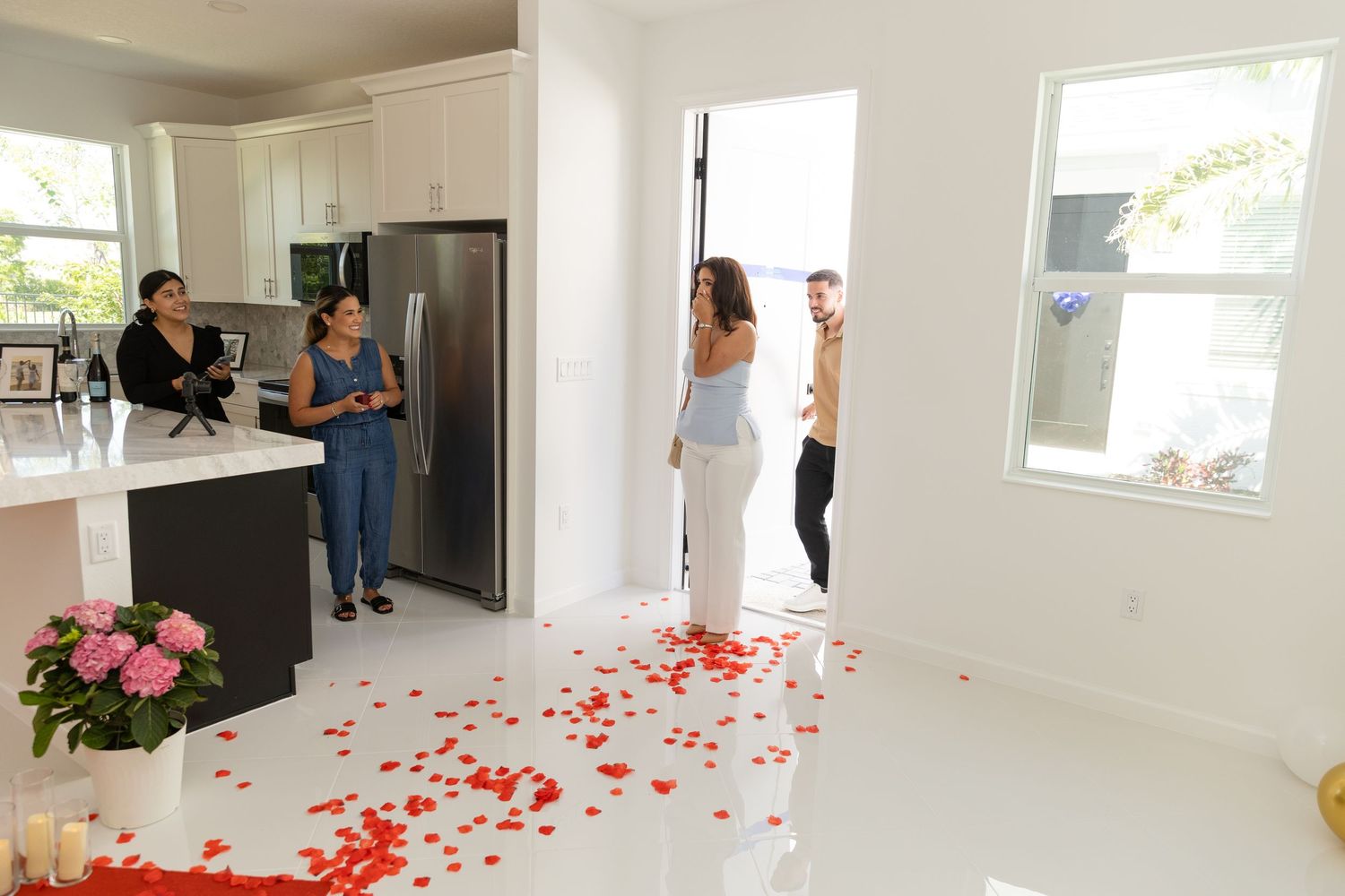 People walk through an empty white modern interior space decorated with scattered red rose petals on the floor.