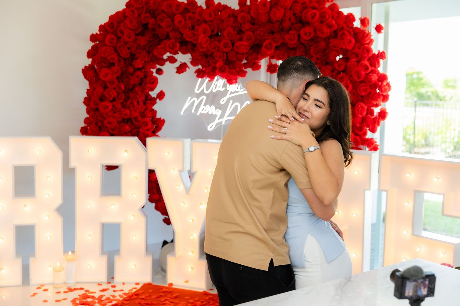 Romantic couple embraces under a beautiful heart-shaped arch made of vibrant red roses and flowers.