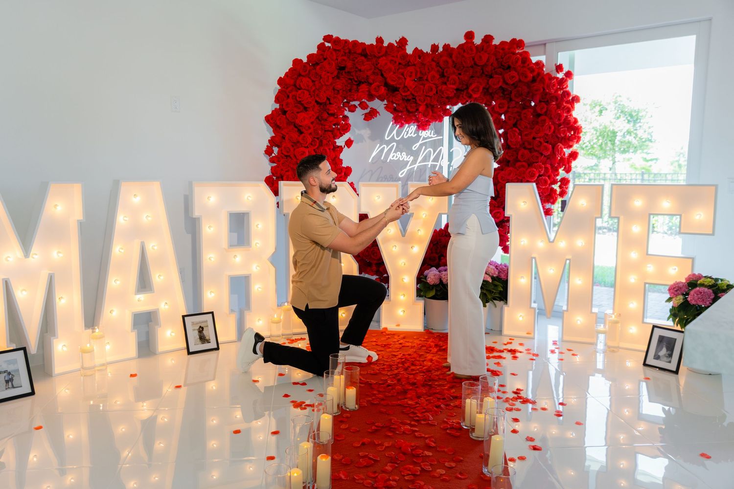 A stunning red flower archway made of roses creates a romantic entrance with illuminated marquee letters in the background.