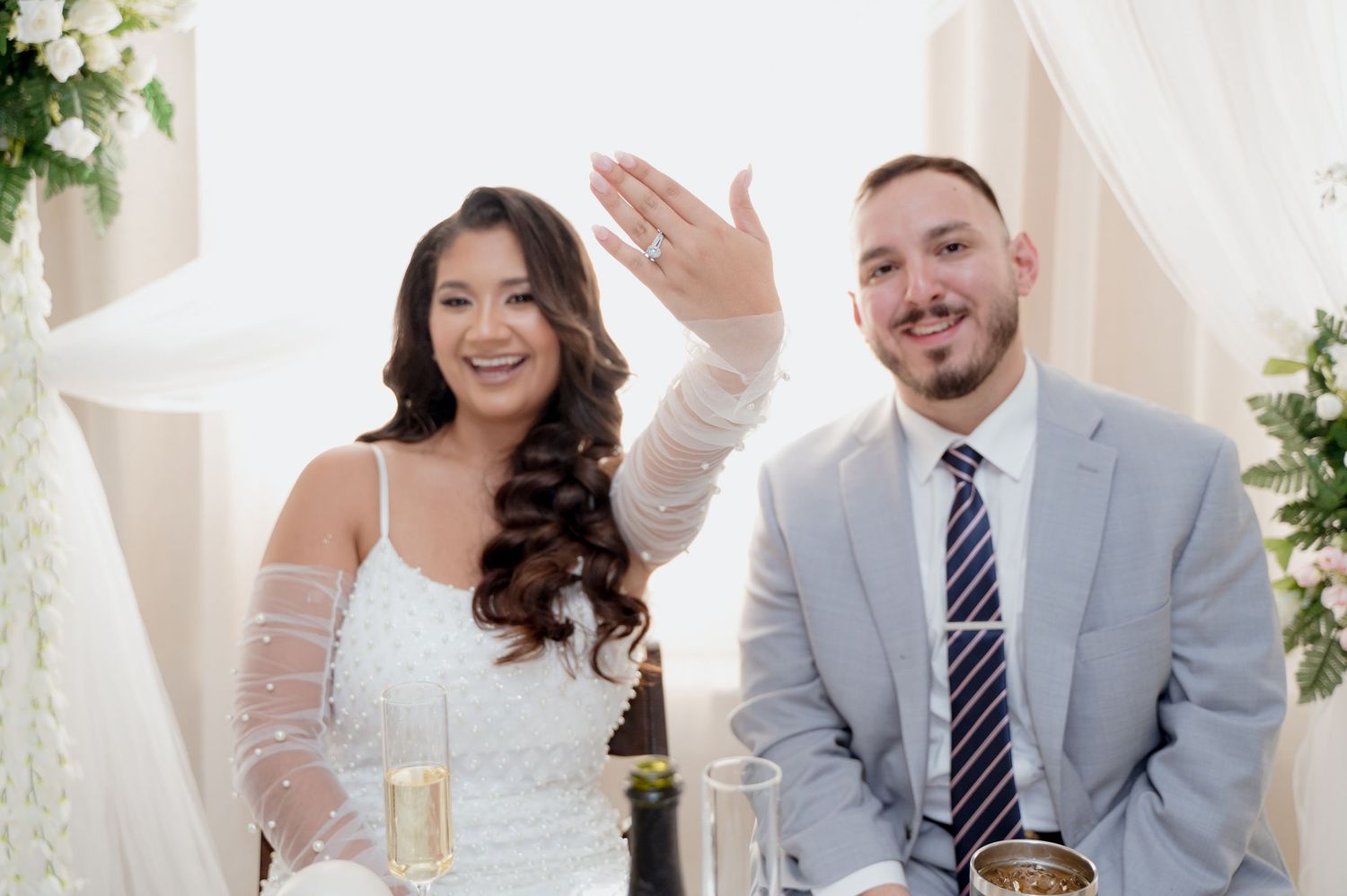 A couple celebrates their wedding day in an elegant white venue decorated with floral arrangements and greenery.