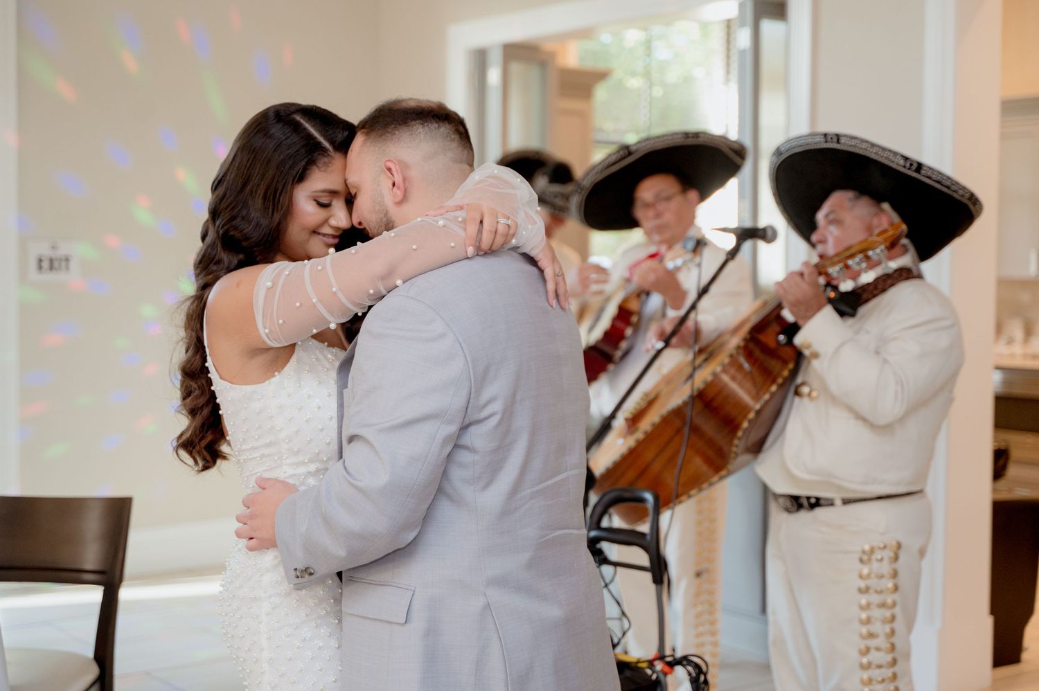 Newlyweds share a romantic dance in a bright ballroom as guests look on during their wedding reception celebration.