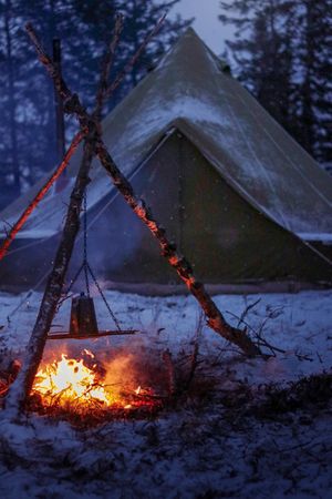Five sequential photos show a campfire gradually igniting against a snowy forest backdrop with teepee tents visible in background.