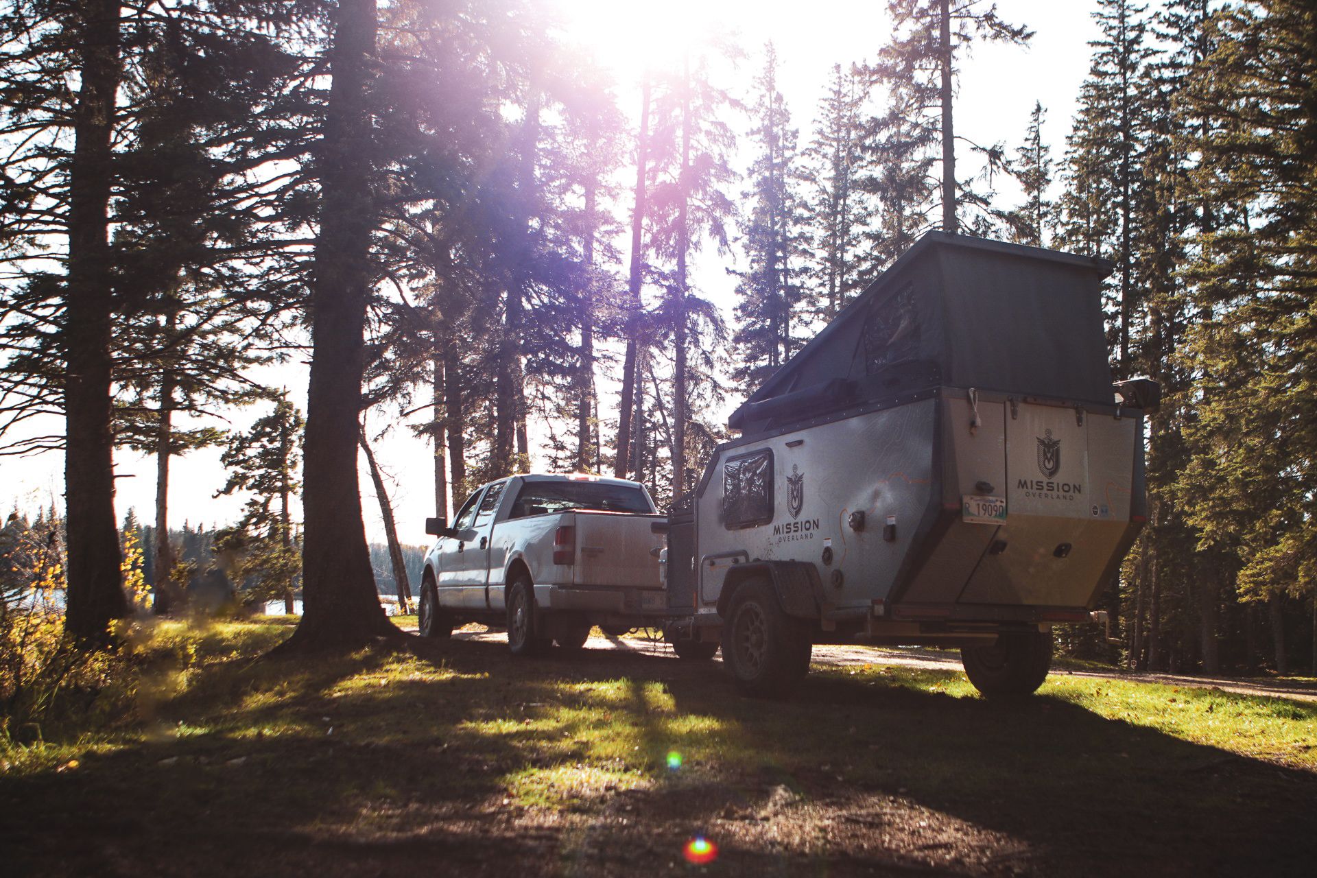 Two overlanding vehicles with rooftop tents parked in a sunlit forest campsite during golden hour.
