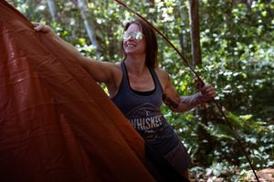 A rock climber scaling a challenging outdoor boulder route through a dense forest canopy.