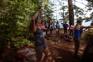 A group of hikers navigate down a steep dirt trail through a forest near the ocean on a sunny day.