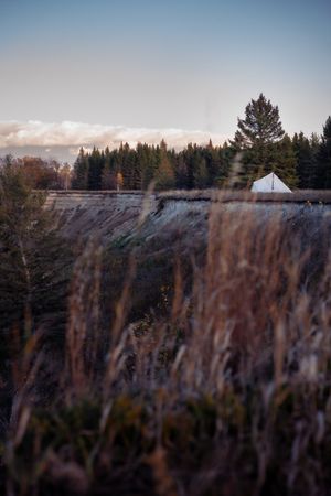 Small white tent visible on distant hilltop against evergreen forest and cloudy sky at sunset.