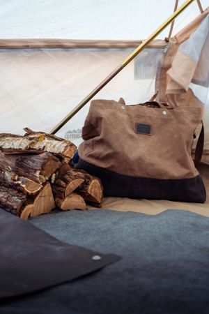 Small pieces of chopped firewood rest next to a brown canvas log carrier on a dark surface.
