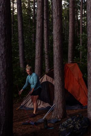 Four sequential photos of a camper setting up a tent at dusk in a wooded forest campsite.
