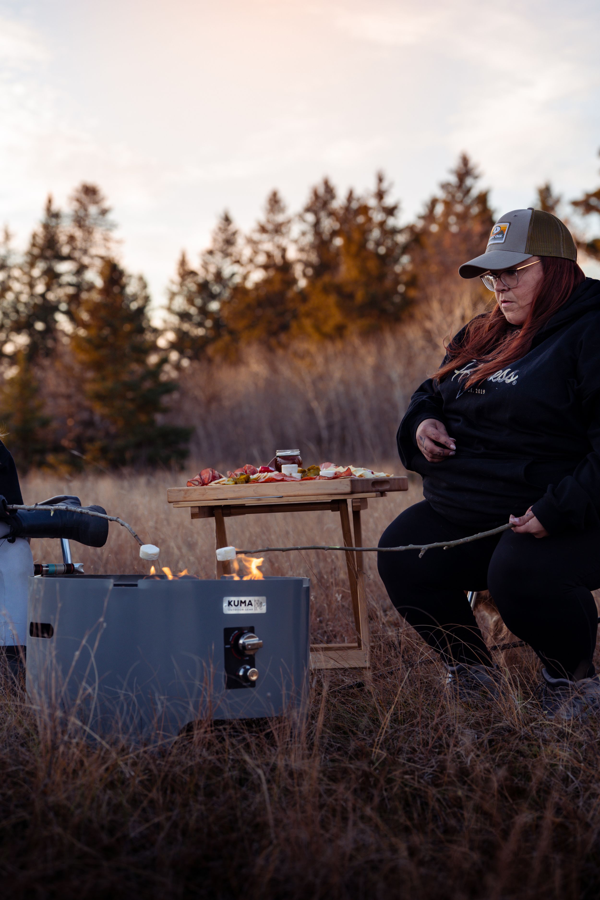 A series of silhouettes show someone sitting at a rustic outdoor table during sunset amongst tall grass and trees.