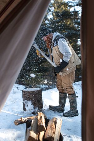 Action sequence shows person chopping wood with an axe in snowy winter setting with evergreen trees in background.