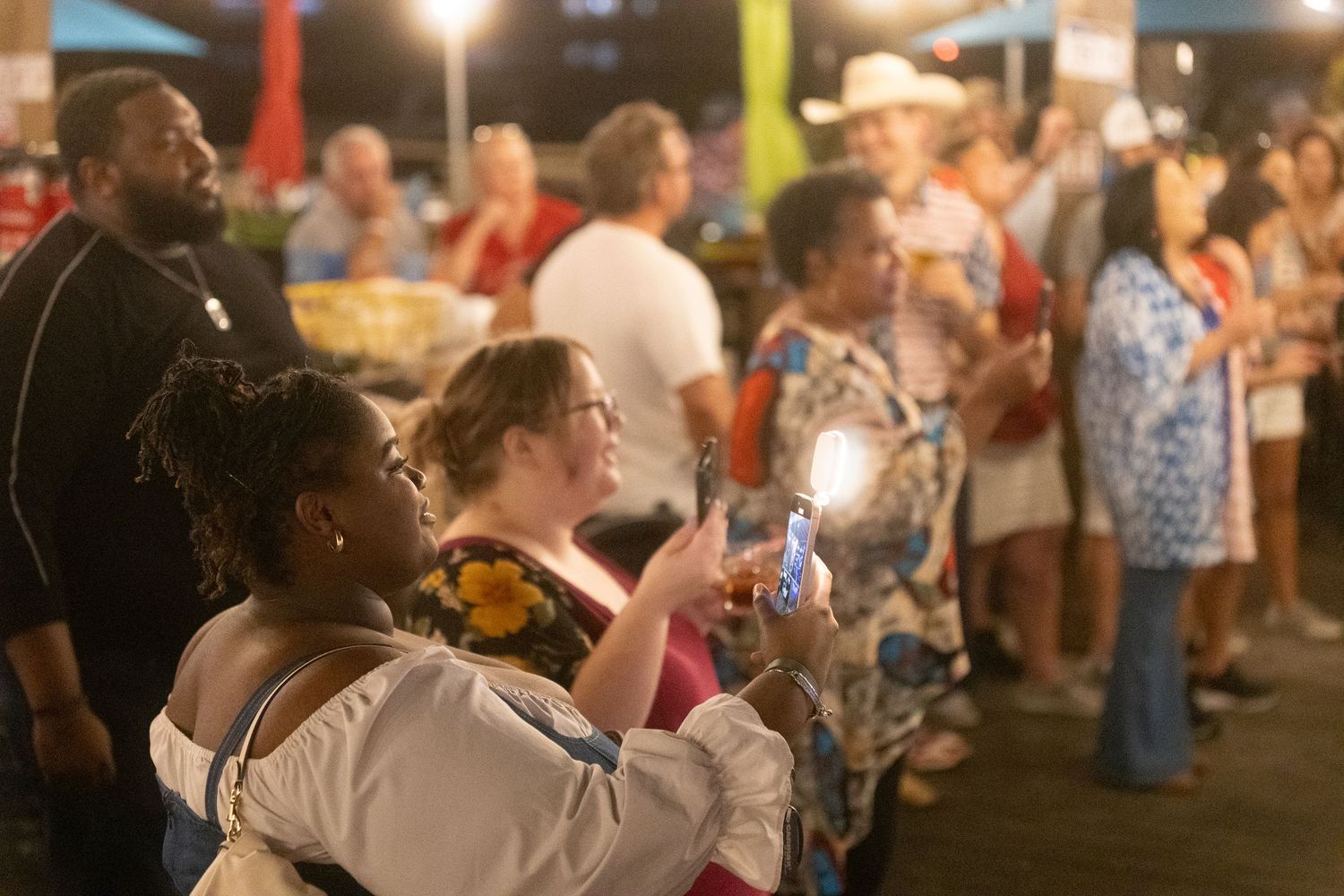 Audience members enjoy an evening outdoor concert under string lights at a summer festival.
